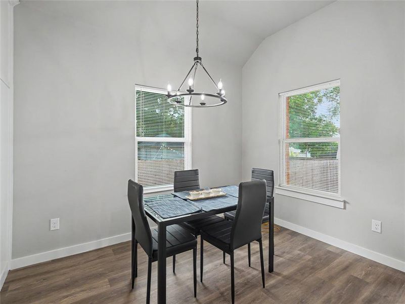Dining area featuring wood-finish flooring, two windows with blinds, a vaulted ceiling, and a modern chandelier Dining area featuring wood-finish flooring, two windows with blinds, a vaulted ceiling, and a modern chandelier