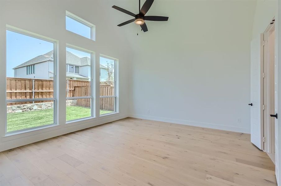 Unfurnished room with ceiling fan, light wood-type flooring, and a towering ceiling