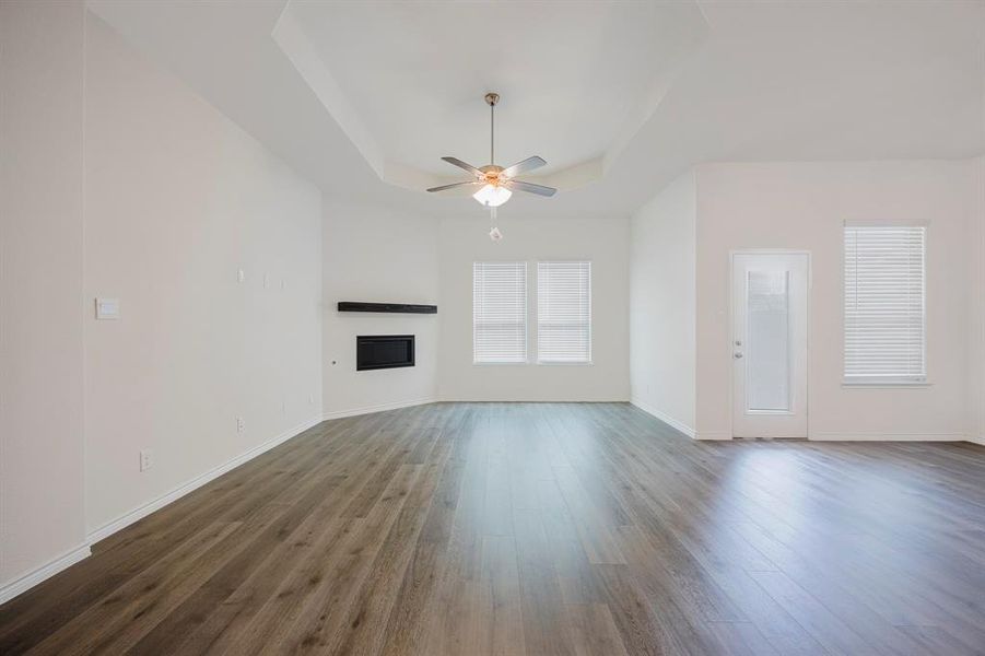 Unfurnished living room featuring a tray ceiling, dark hardwood / wood-style floors, and ceiling fan