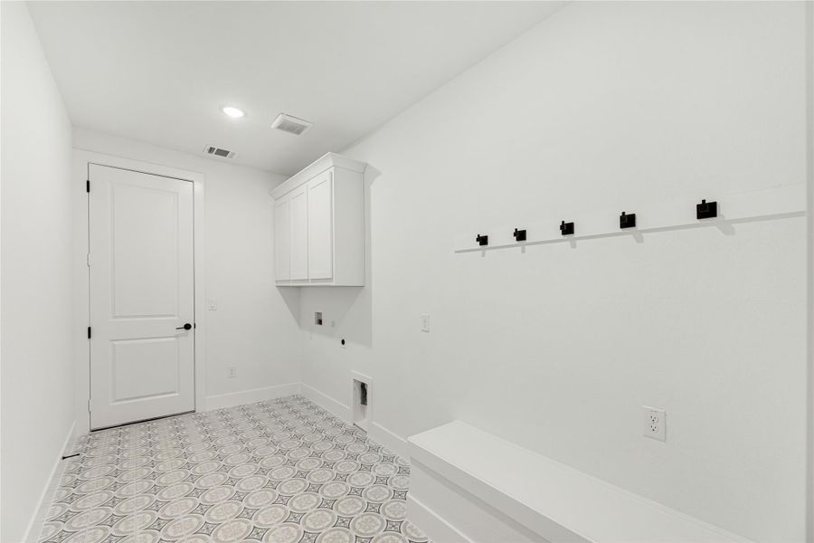 Mudroom with patterned tile floor, built-in bench, black wall hooks, and white upper cabinets