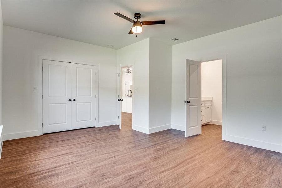Unfurnished bedroom featuring light wood finished floors, a ceiling fan, ensuite bathroom, and a closet