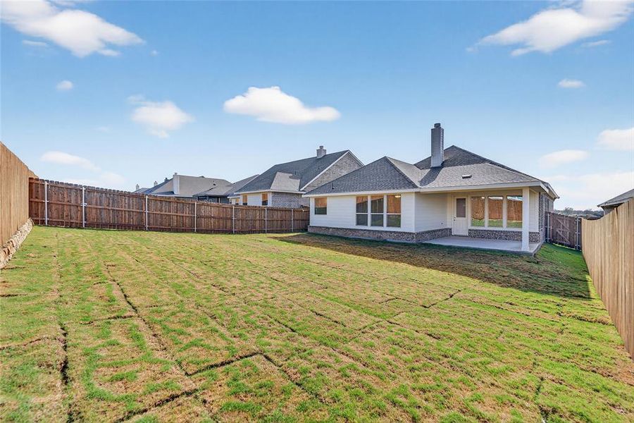 Back of house featuring a chimney, a fenced backyard, a patio area, a shingled roof, and stone siding