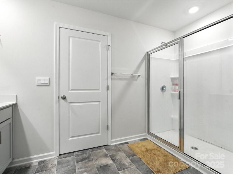 Spacious walk-in shower with tile surround and glass door. Built-in shelving niche and modern fixtures provide both style and functionality in this well-designed primary bathroom.