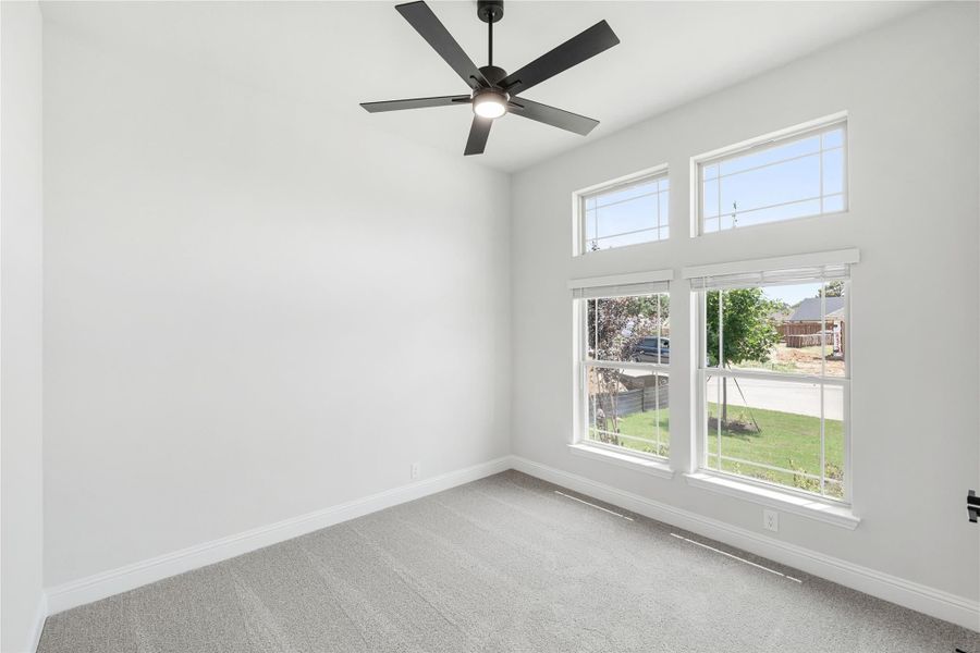 Empty bedroom with gray carpet, black ceiling fan, and large windows with yard view