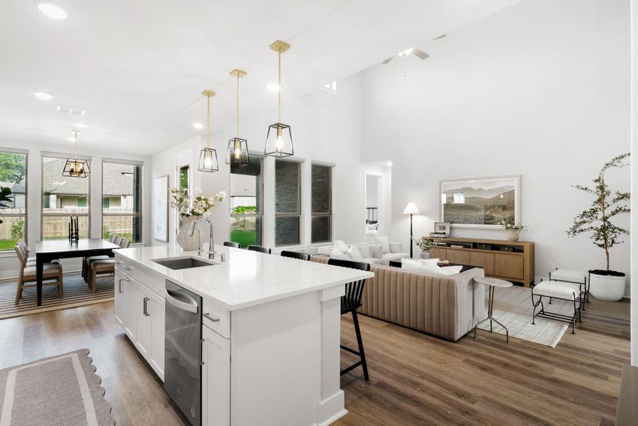 An open concept living area features soaring ceilings and wood flooring, connecting a spacious kitchen and comfortable family room.