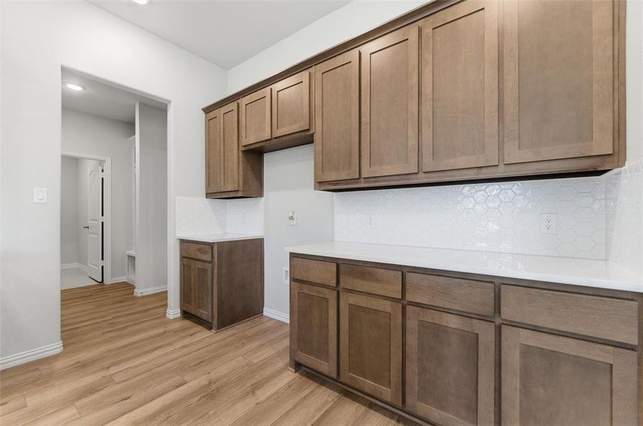 Kitchen featuring backsplash, light wood finished floors, brown cabinets, light stone counters, and recessed lighting