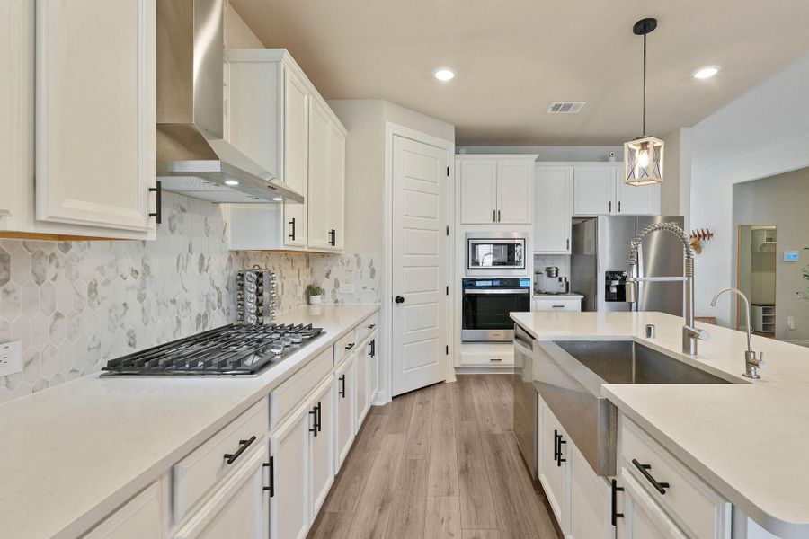 This modern kitchen features sleek white cabinetry, a large farmhouse sink, and stainless steel appliances. The hexagonal tile backsplash adds a stylish touch, and the spacious countertops offer plenty of workspace. A contemporary light fixture and wood flooring complete the look. This modern kitchen features sleek white cabinetry, a large farmhouse sink, and stainless steel appliances. The hexagonal tile backsplash adds a stylish touch, and the spacious countertops offer plenty of workspace. A contemporary light fixture and wood flooring complete the look.