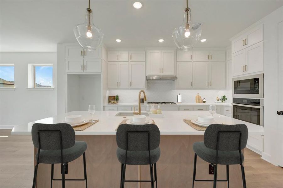 Spacious kitchen featuring a large island, white cabinetry, integrated stainless steel appliances, pendant lighting, and wood-finish flooring