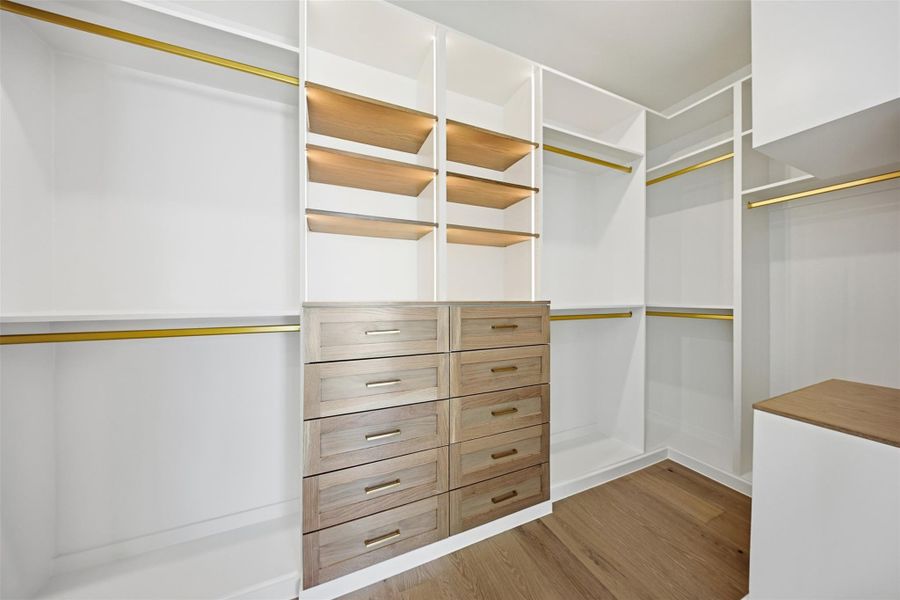 Same floorplan - different finishes. The custom closet system offers ample storage with integrated LED-lit shelving, gold hanging rods, and a central dresser unit.