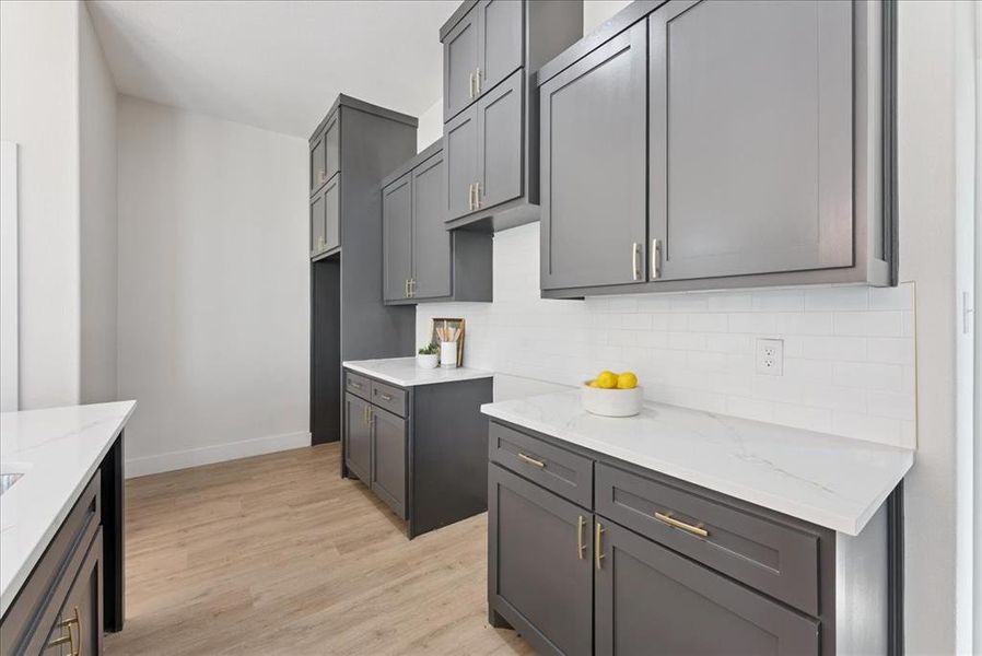 Kitchen featuring tasteful backsplash, light wood finished floors, light stone countertops, and gray cabinetry