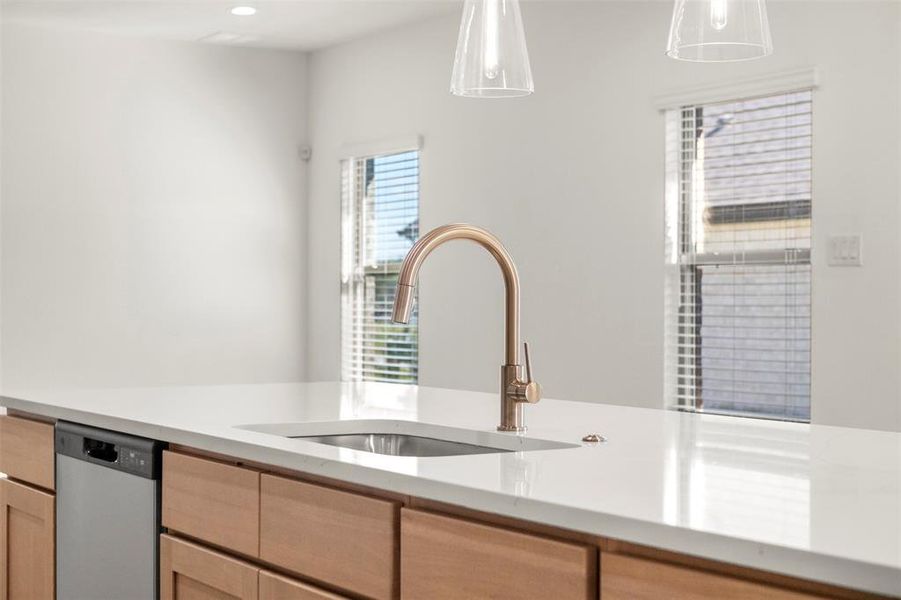 Kitchen with light brown cabinets, dishwasher, light stone counters, and decorative light fixtures
