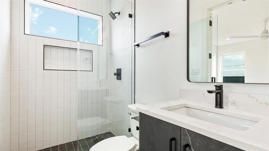 Bathroom featuring a tile shower, vanity, a healthy amount of sunlight, and toilet