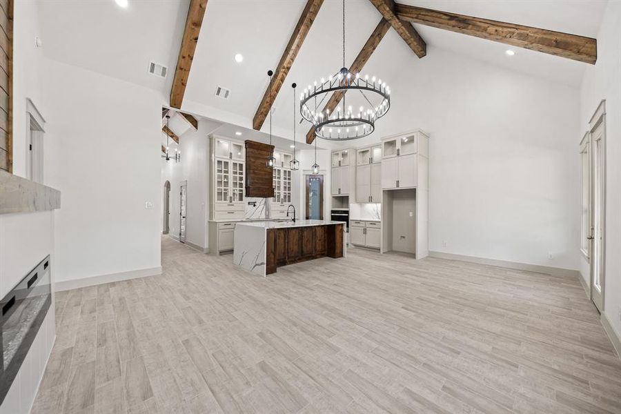 Kitchen with glass insert cabinets, high vaulted ceiling, a center island with sink, recessed lighting, and light wood-style floors