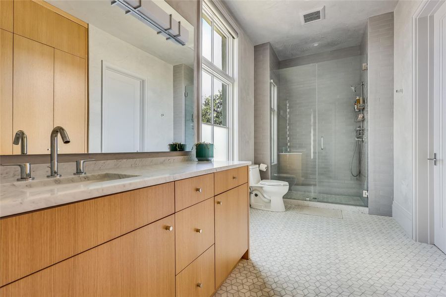 Sleek vanity with marble counters and dual chrome faucets complement this light-filled bath.