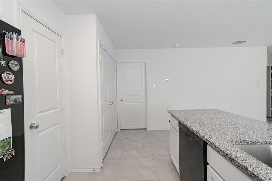 Kitchen with light stone countertops, white cabinets, black appliances, and light tile patterned flooring