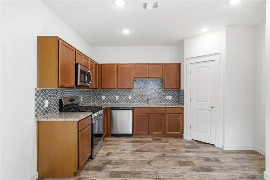Kitchen featuring appliances with stainless steel finishes, light stone counters, brown cabinets, light wood-style floors, and recessed lighting Kitchen featuring appliances with stainless steel finishes, light stone counters, brown cabinets, light wood-style floors, and recessed lighting