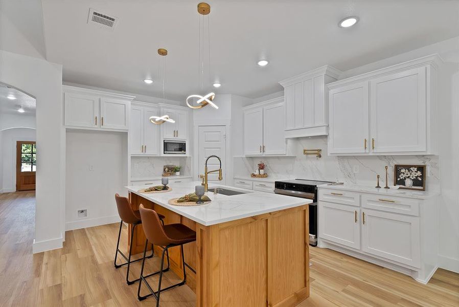 Kitchen with arched walkways, electric range, decorative light fixtures, white cabinetry, and recessed lighting