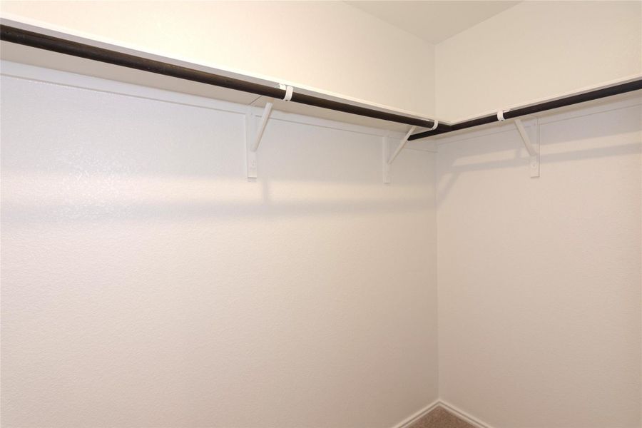 Walk-in closet featuring white painted walls, corner shelving, and multiple clothing rods