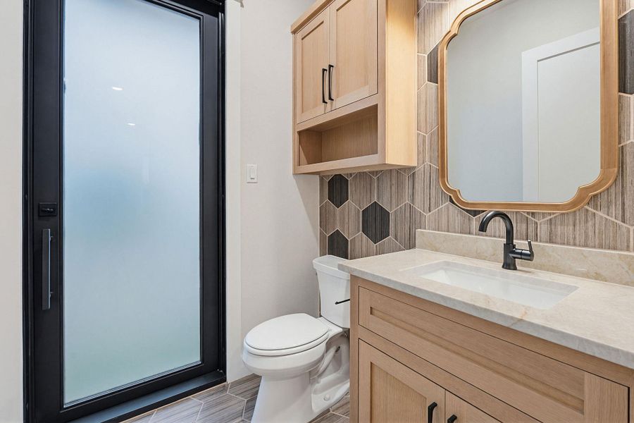 Frosted glass door with black trim, vanity with light wood cabinetry, stone countertop, matte black faucet, and a decorative mirror