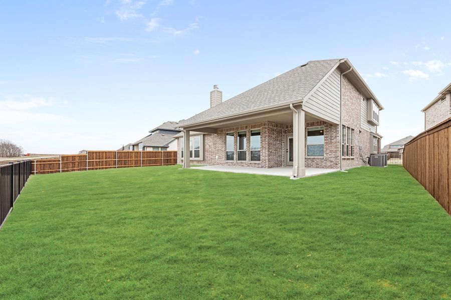 Rear view of two-story brick home with covered patio, large fenced backyard, and green lawn Rear view of two-story brick home with covered patio, large fenced backyard, and green lawn