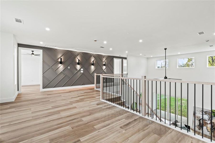Upper-level landing featuring wood-finish flooring, recessed lighting, and a decorative accent wall with sconces