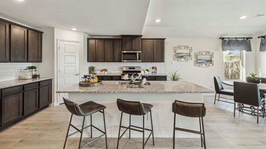 The kitchen features dark wood cabinetry, light-colored countertops, a large center island with seating, and stainless steel appliances