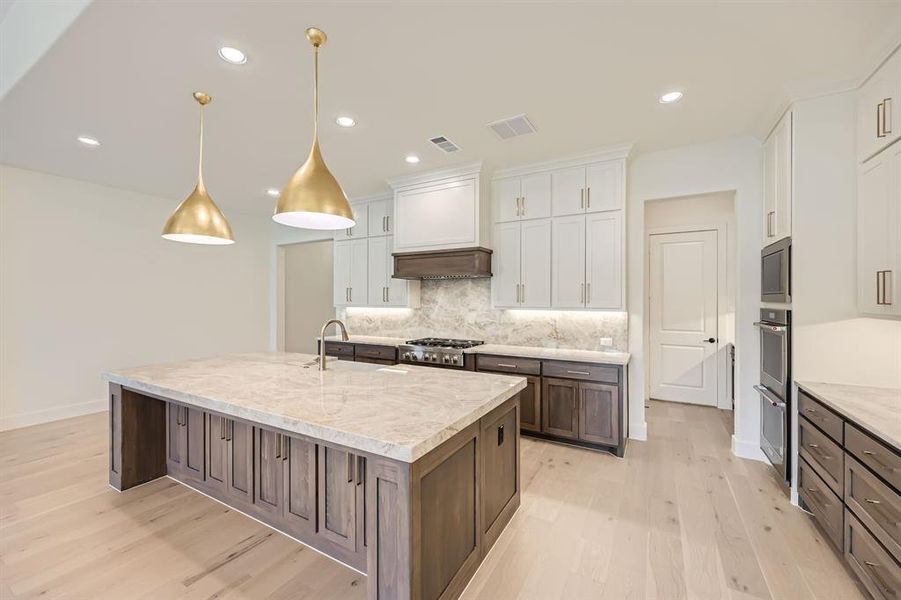 Kitchen featuring an island with sink, stainless steel appliances, pendant lighting, white cabinetry, and light hardwood / wood-style floors