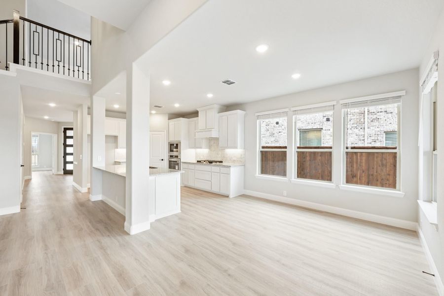 Open-concept living area with light wood floors, white kitchen, and second-floor balcony overlook Open-concept living area with light wood floors, white kitchen, and second-floor balcony overlook