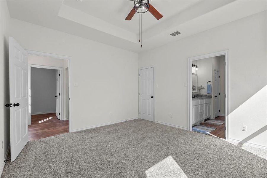 Unfurnished bedroom featuring ensuite bath, ceiling fan, a raised ceiling, and carpet flooring