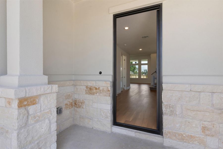 Entryway featuring a black-framed glass door, stone veneer wainscoting, a stucco column, and concrete flooring