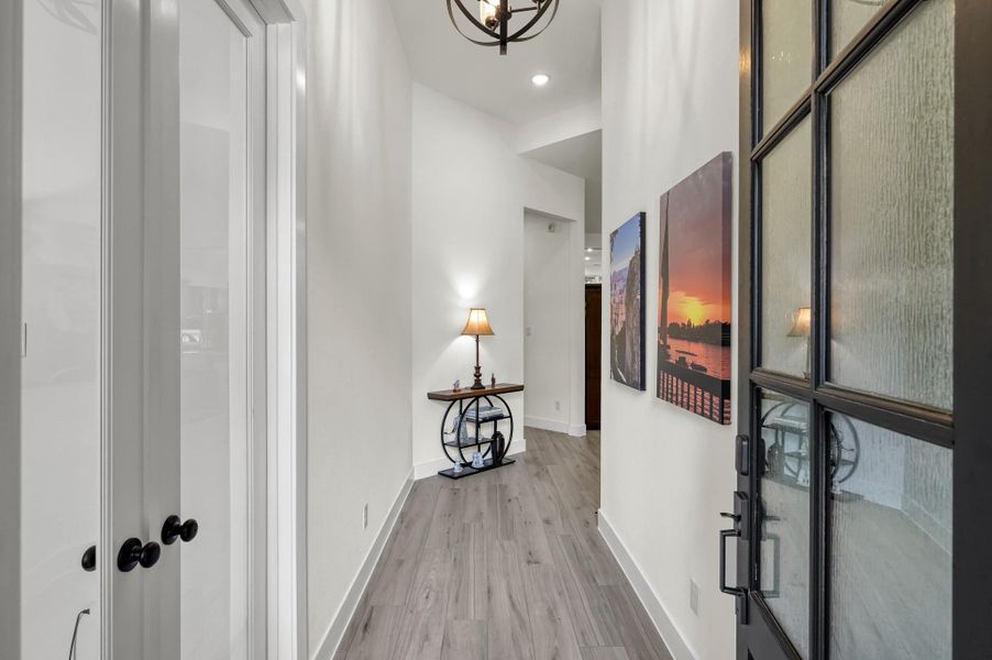Bright and welcoming entry hallway featuring upgraded wood-look tile flooring and modern finishes throughout. To the left, elegant French doors lead into the private home office