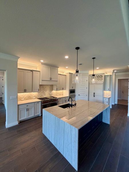Rich hardwood flooring complements a waterfall island in this masterfully crafted culinary space.