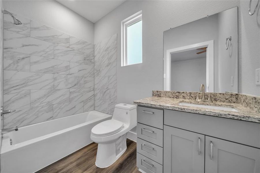 Full bathroom with wood-type flooring, toilet, tiled shower / bath combo, and vanity