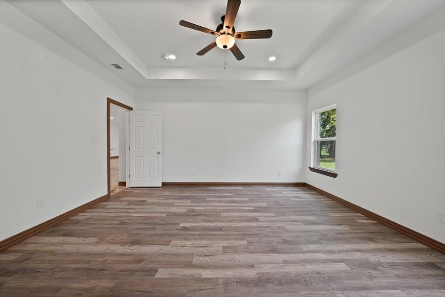 Spare room with a tray ceiling, ceiling fan, wood finished floors, and recessed lighting
