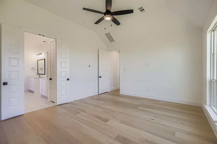 Unfurnished bedroom with lofted ceiling, light wood finished floors, ensuite bath, and a ceiling fan