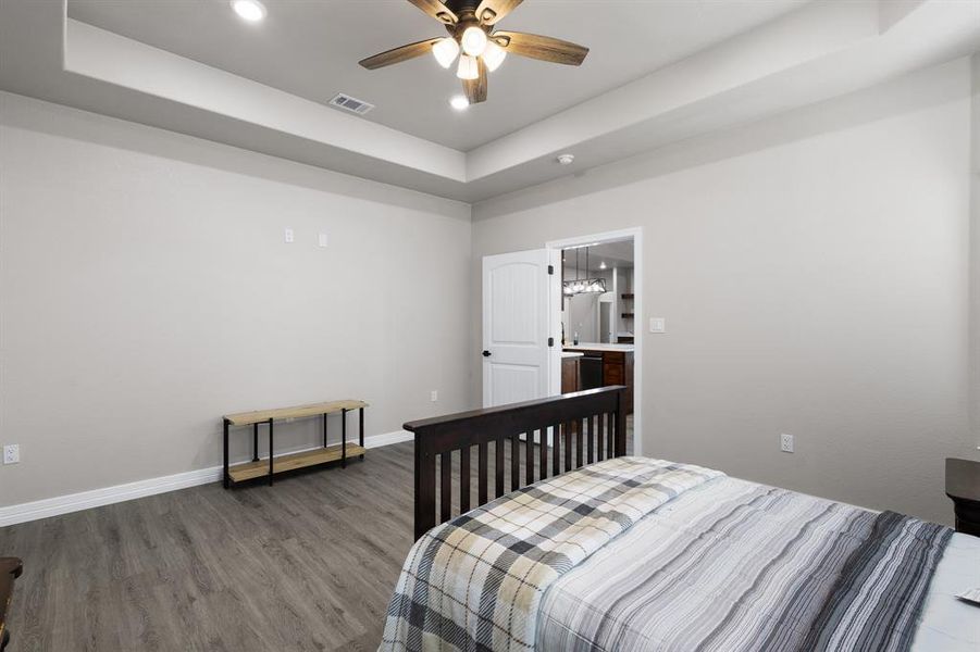 Bedroom with a tray ceiling, recessed lighting, wood finished floors, ceiling fan, and ensuite bathroom