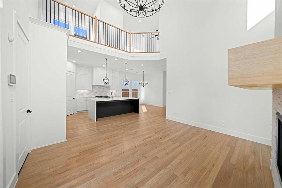 Unfurnished living room with a chandelier, light wood-style floors, a fireplace, recessed lighting, and a high ceiling Unfurnished living room with a chandelier, light wood-style floors, a fireplace, recessed lighting, and a high ceiling