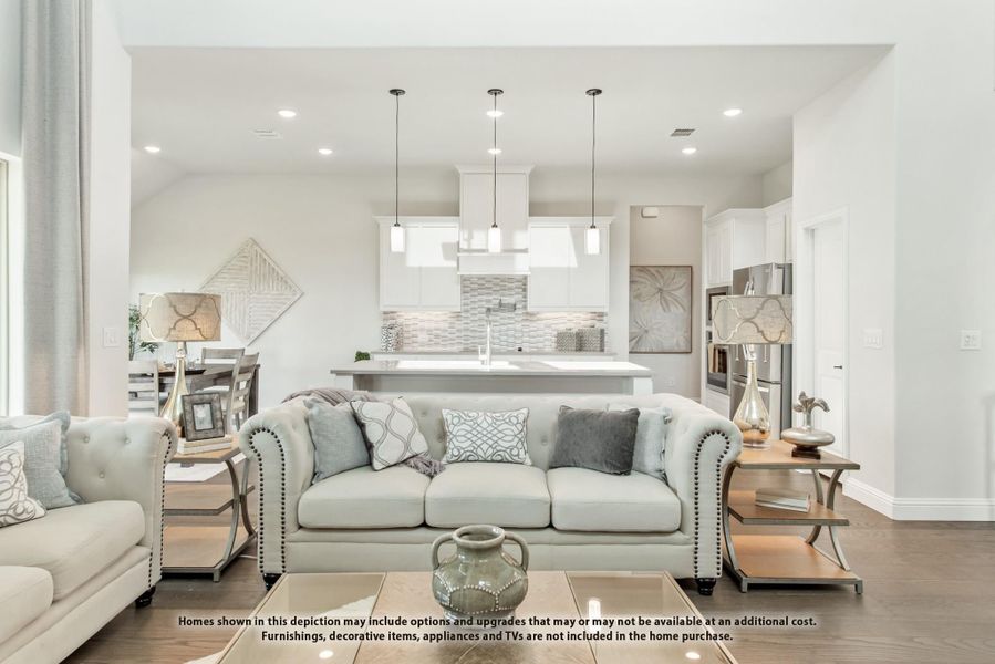 Open-concept living room with tufted sofa and view into white kitchen with pendant lights and island Open-concept living room with tufted sofa and view into white kitchen with pendant lights and island
