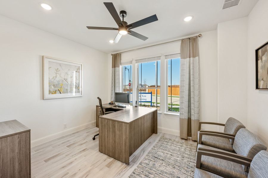 Home office with wood desk, ceiling fan, light hardwood floors, and large windows with curtains
