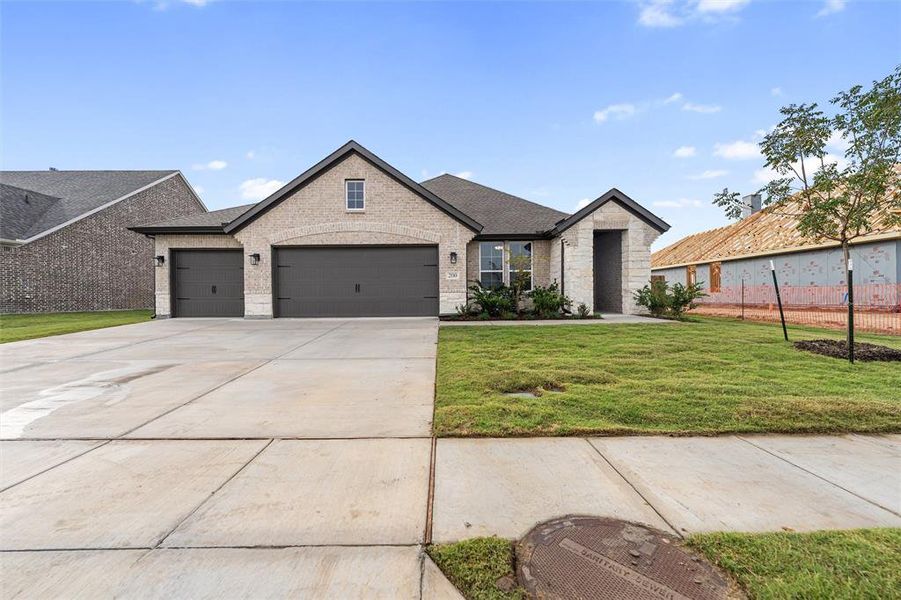View of front of property with a front lawn, concrete driveway, a garage, stone siding, and brick siding View of front of property with a front lawn, concrete driveway, a garage, stone siding, and brick siding