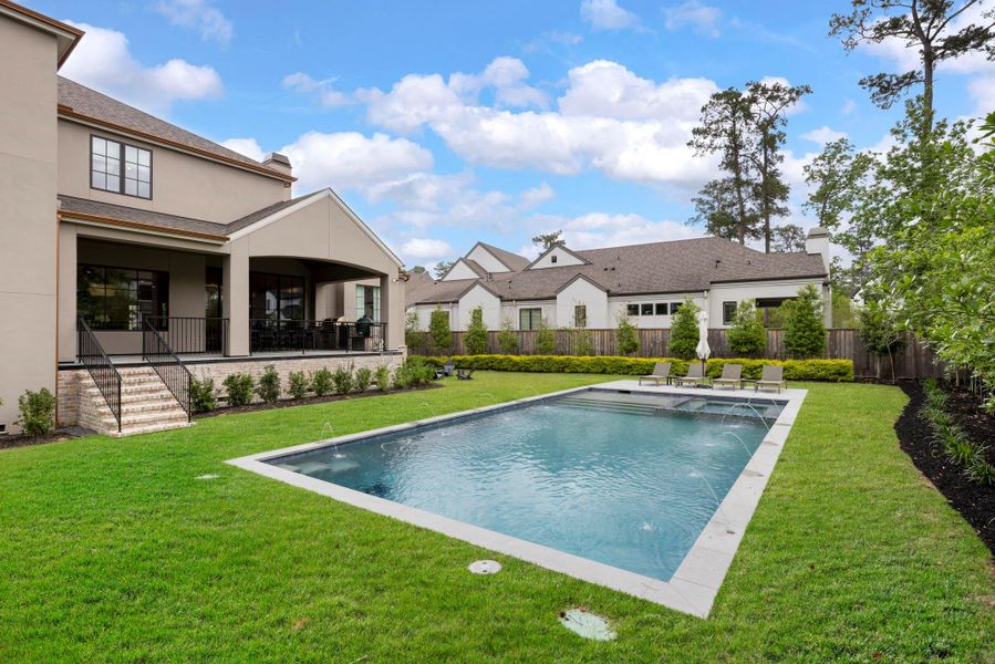 Well-appointed outdoor living space featuring a pool with water features, expansive lawn, and a covered patio with outdoor kitchen—perfect for hosting family and guests.