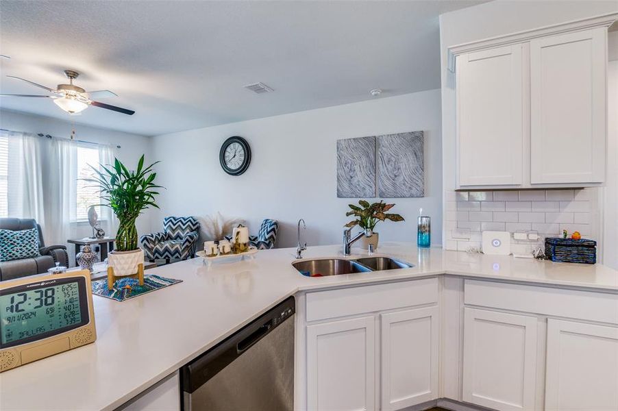 Kitchen with white cabinetry, dishwasher, sink, backsplash, and kitchen peninsula