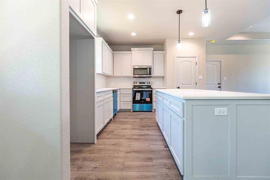 Kitchen with decorative backsplash, appliances with stainless steel finishes, pendant lighting, light wood-style flooring, and white cabinets