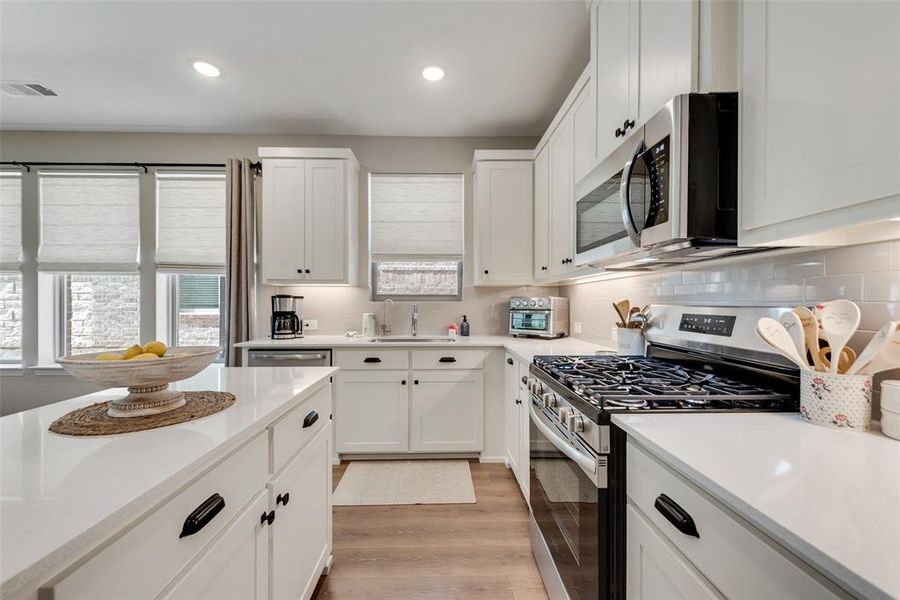 Modern kitchen featuring an island, white cabinetry, integrated stainless steel appliances, with upgraded Pergo water tight laminate wood look flooring, and recessed lighting Modern kitchen featuring an island, white cabinetry, integrated stainless steel appliances, with upgraded Pergo water tight laminate wood look flooring, and recessed lighting