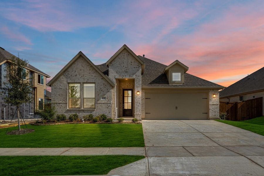 Single-story brick home with two-car garage, covered entry, and manicured front lawn at dusk Single-story brick home with two-car garage, covered entry, and manicured front lawn at dusk