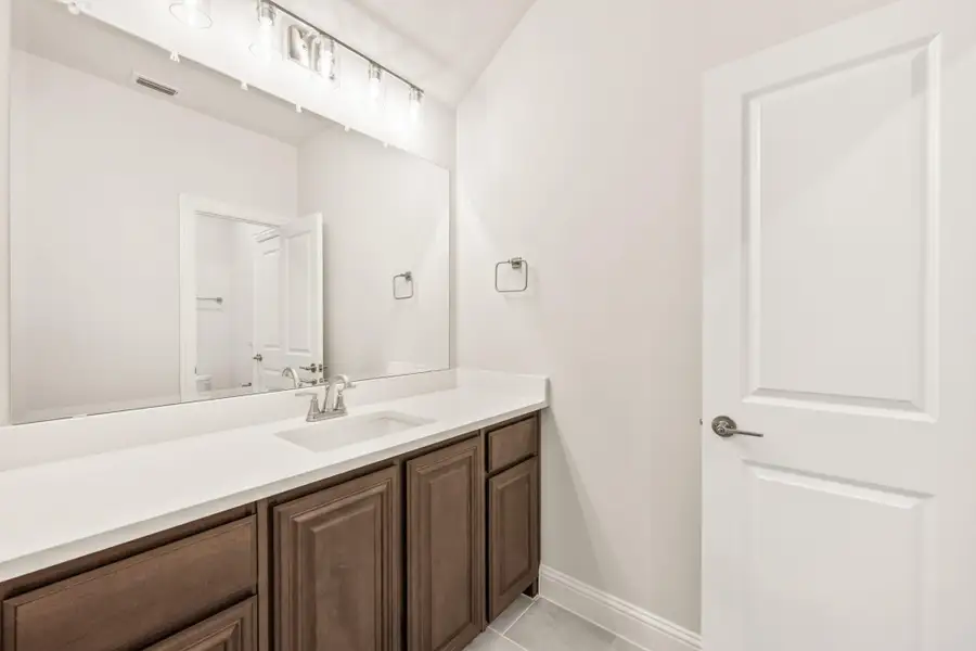 Bathroom vanity with dark wood cabinets, white countertop, large mirror, and lighted fixture above sink