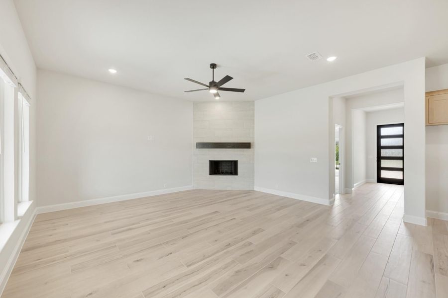 Empty living room with light wood floors, tile fireplace, and ceiling fan