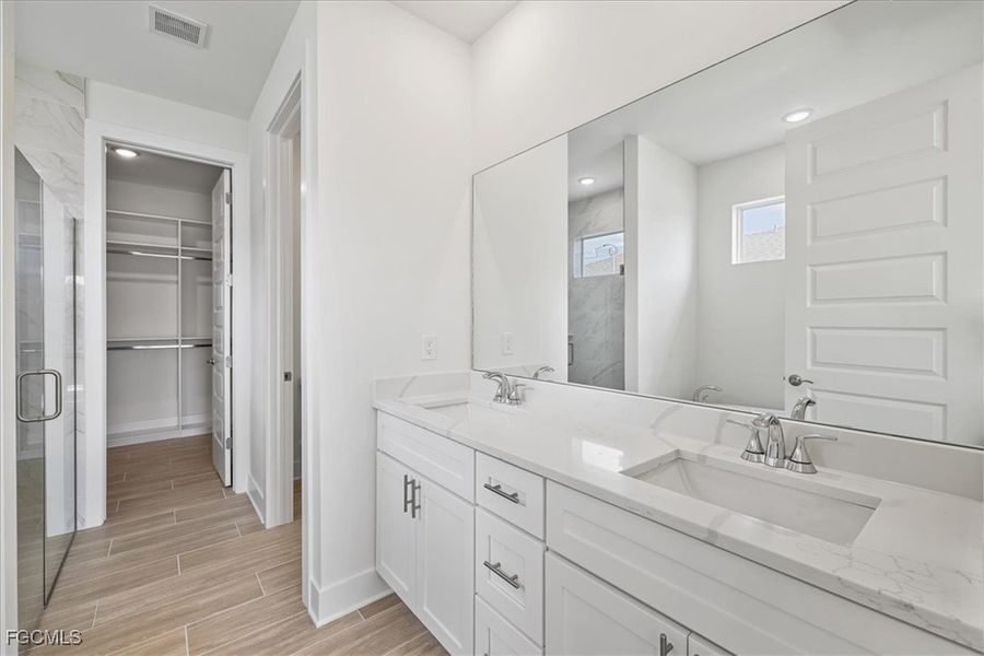Full bath featuring double vanity, wood finish floors, a walk in closet, a shower stall, and recessed lighting