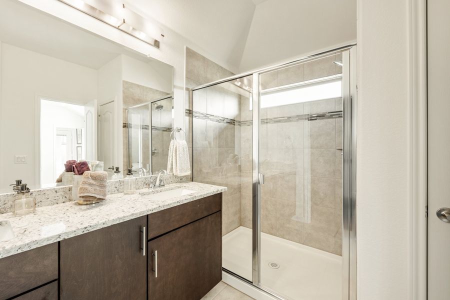 Bathroom with dark wood vanity, granite countertop, large mirror, and glass-enclosed tile shower