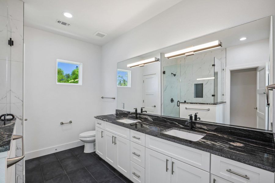 Granite counters and dark floor tiles elevate this spacious primary bathroom design.